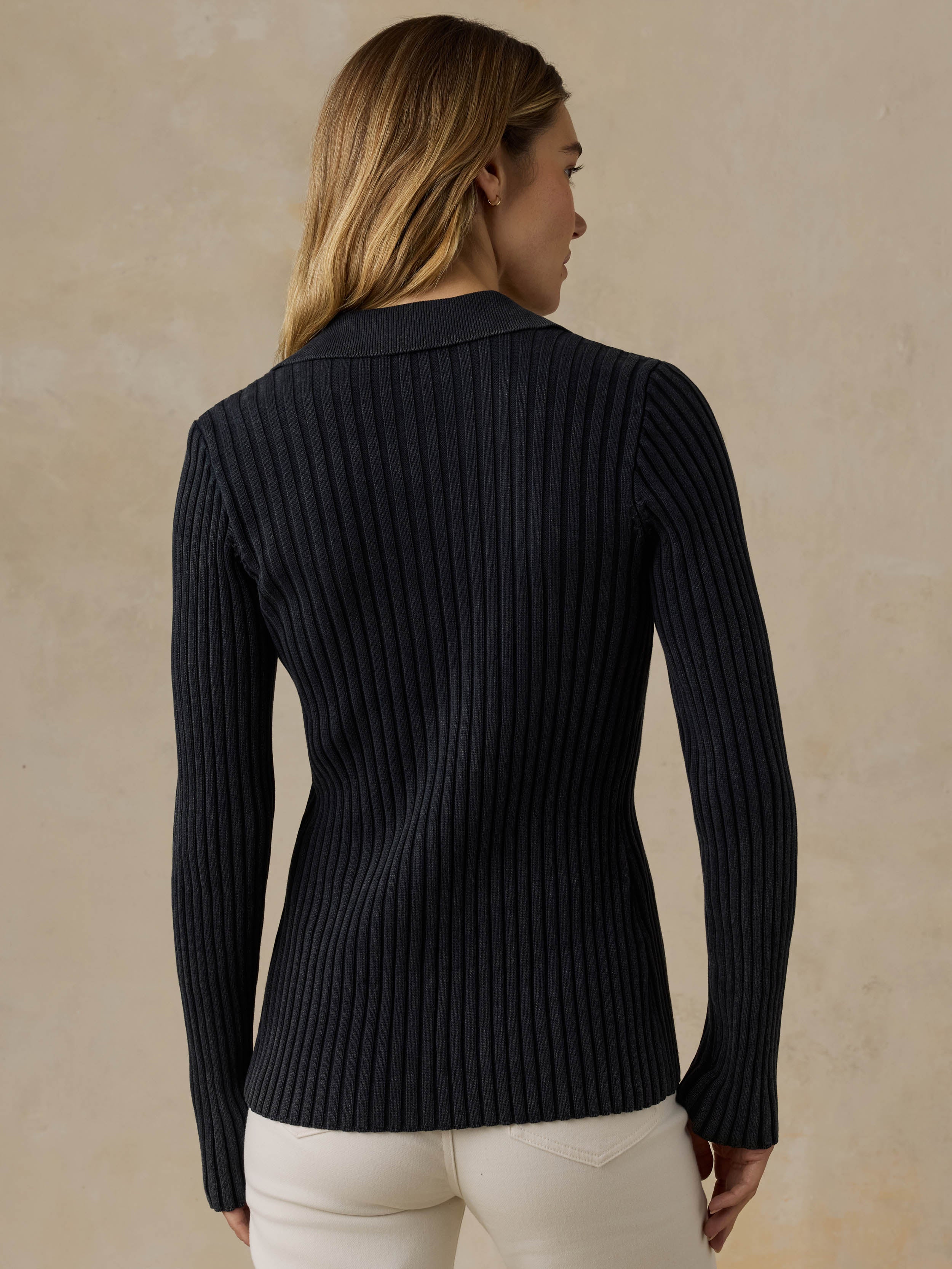 Woman wearing a black ribbed cardigan and white pants against a beige background