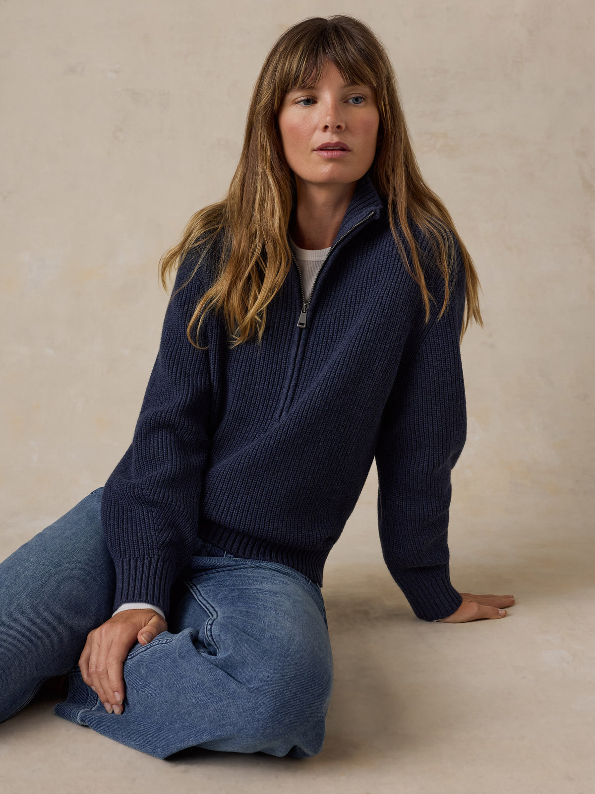 Woman wearing a navy blue quarter zip sweater and blue jeans, image 1 of 6