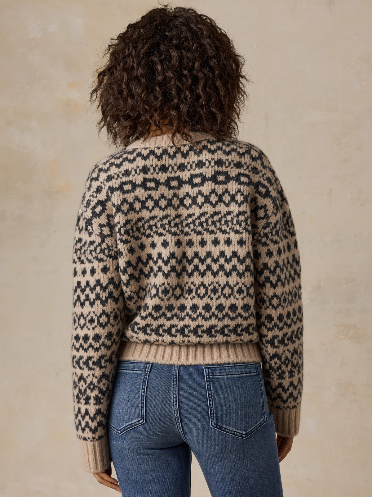 A woman viewed from behind wearing a beige printed sweater and blue jeans, image 5 of 7