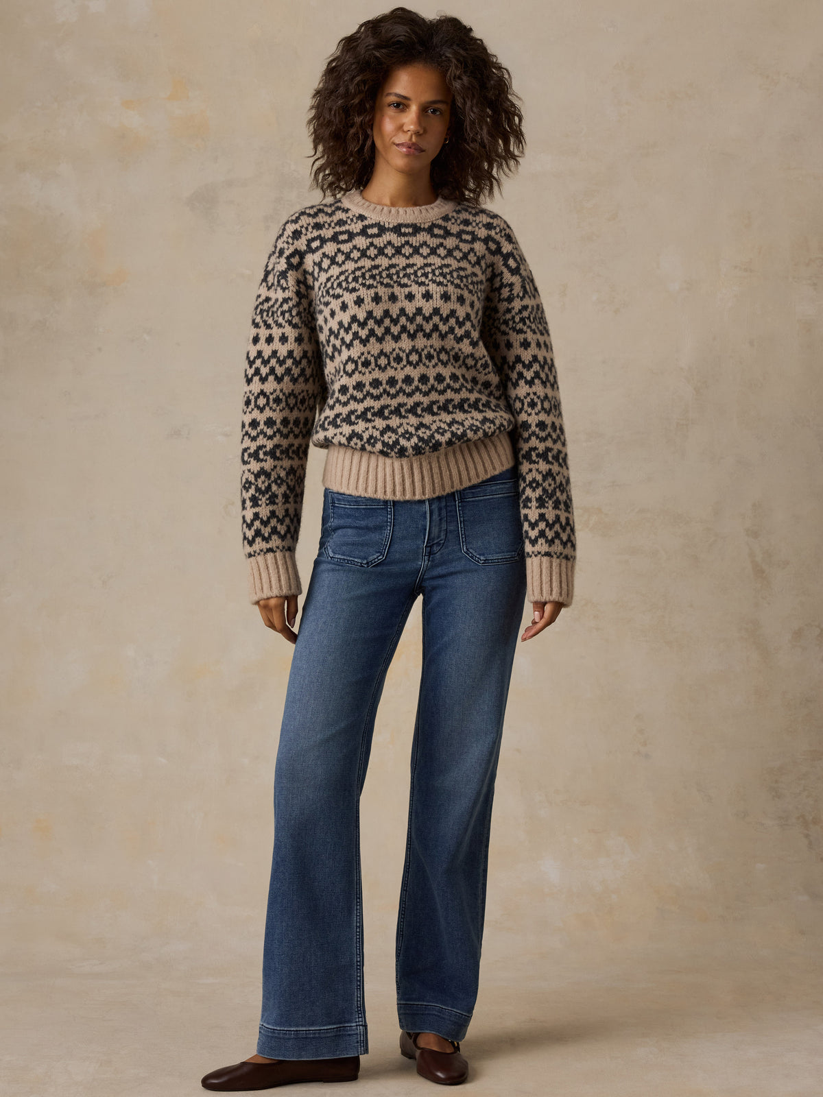 A woman wearing a beige printed sweater, blue jeans, and flats, image 2 of 7