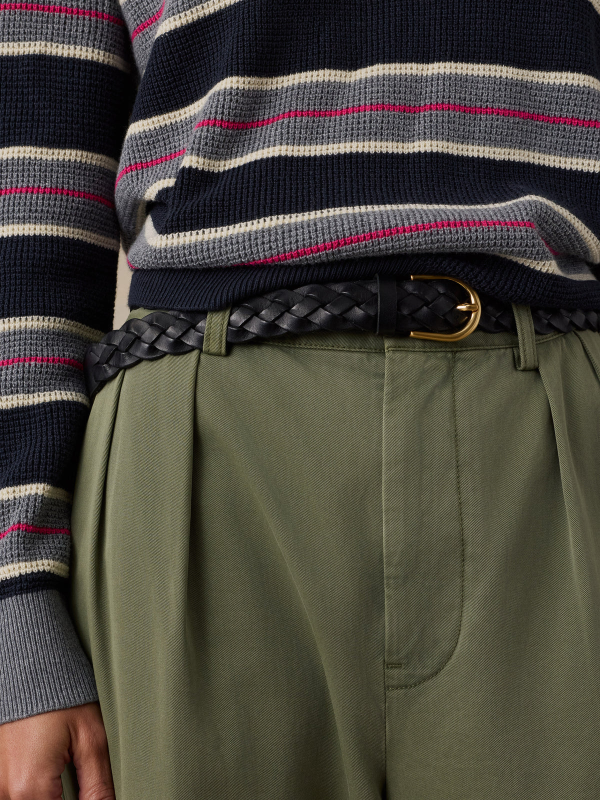 Close-up of a woan wearing olive green pleated trousers, a black braided belt with a gold buckle, and a navy sweater with gray, beige, and pink horizontal stripes., image 4 of 5