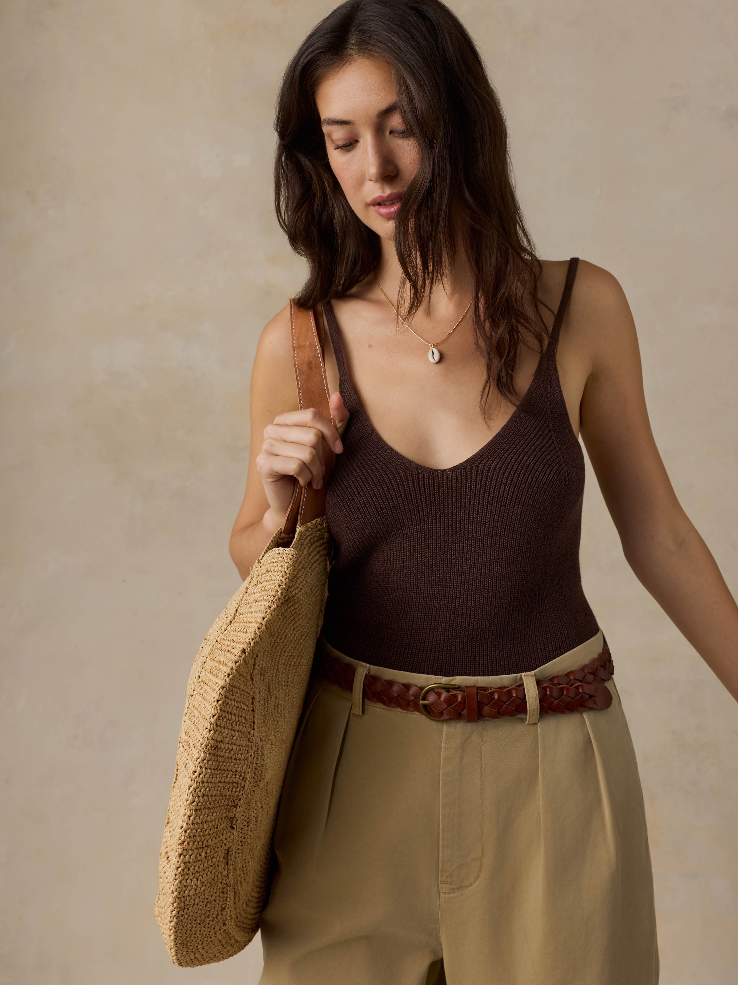 Woman wearing a brown tank top and beige pants against a beige background