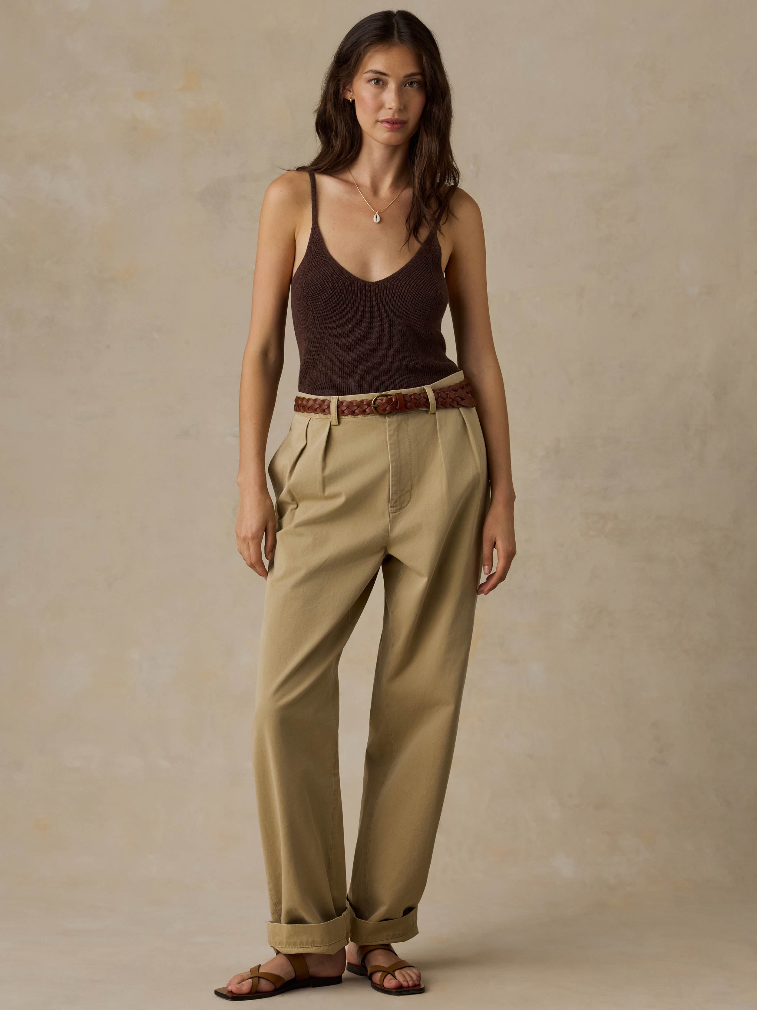 Woman wearing a brown tank top and beige pants against a beige background