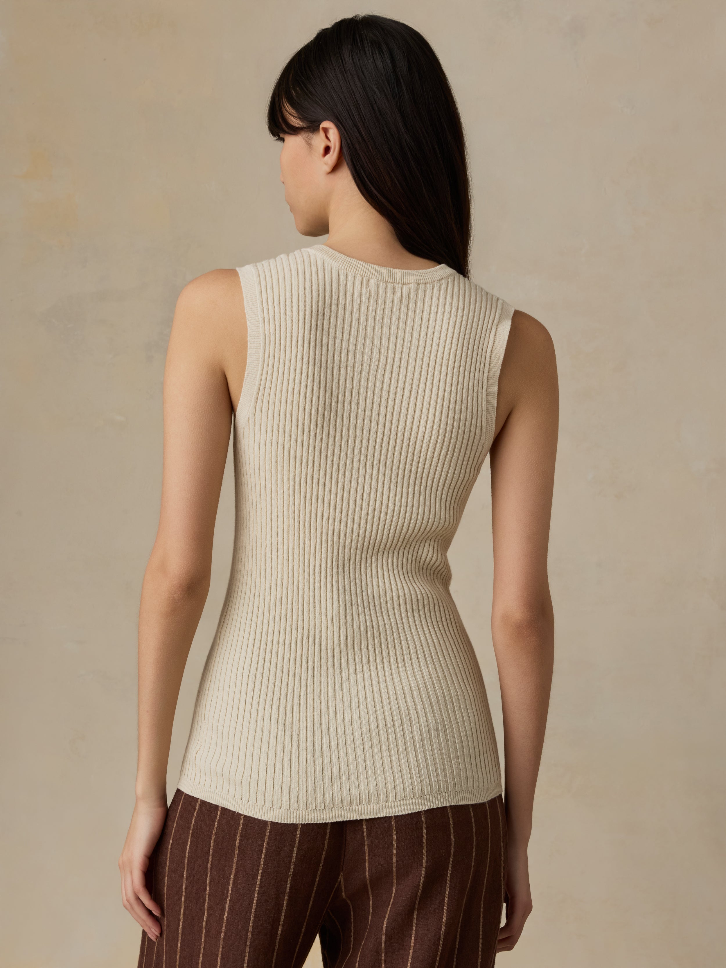 Woman wearing a beige ribbed knit sleeveless top against a beige background