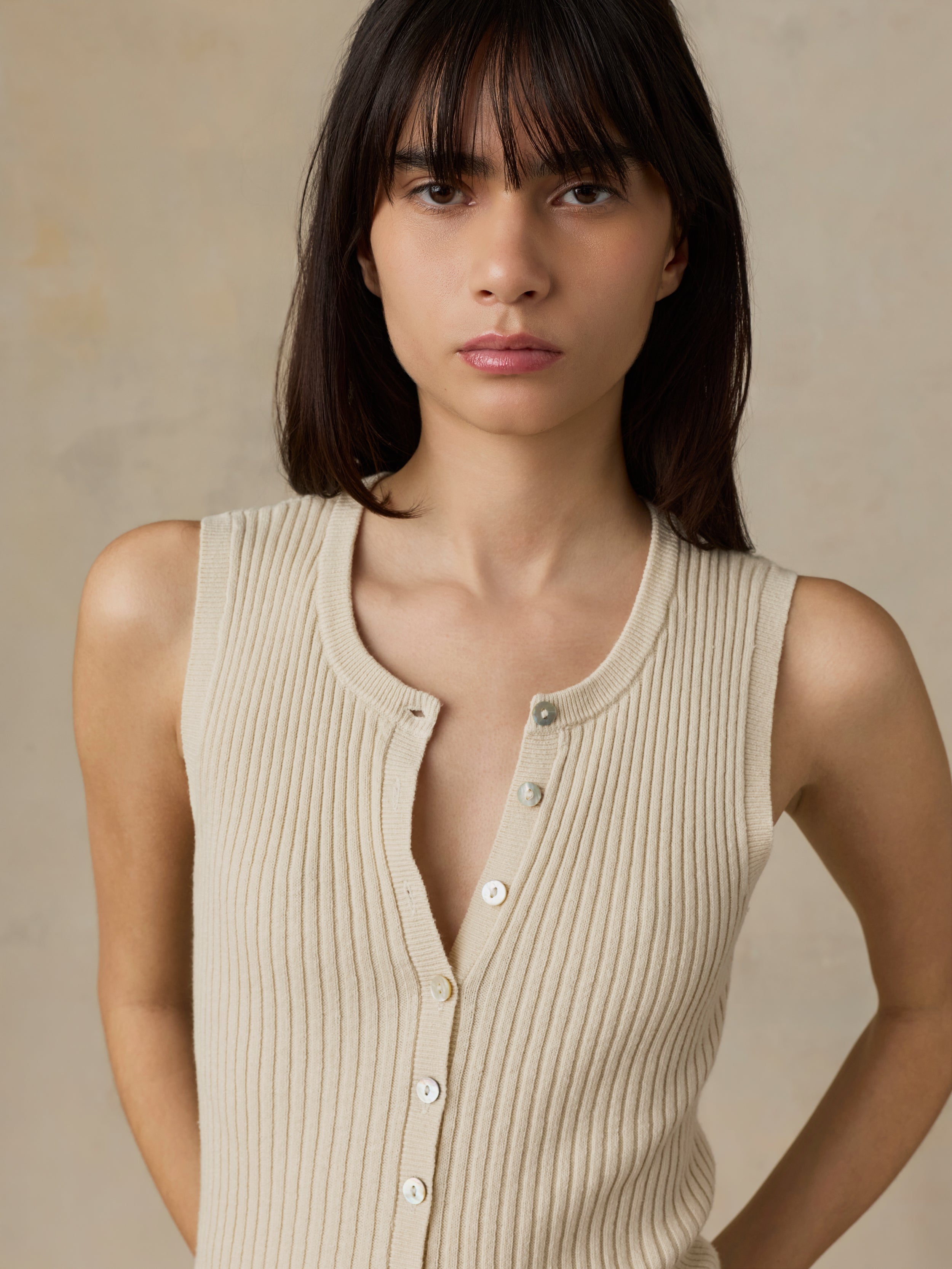 Woman wearing a beige ribbed tank top against a neutral background