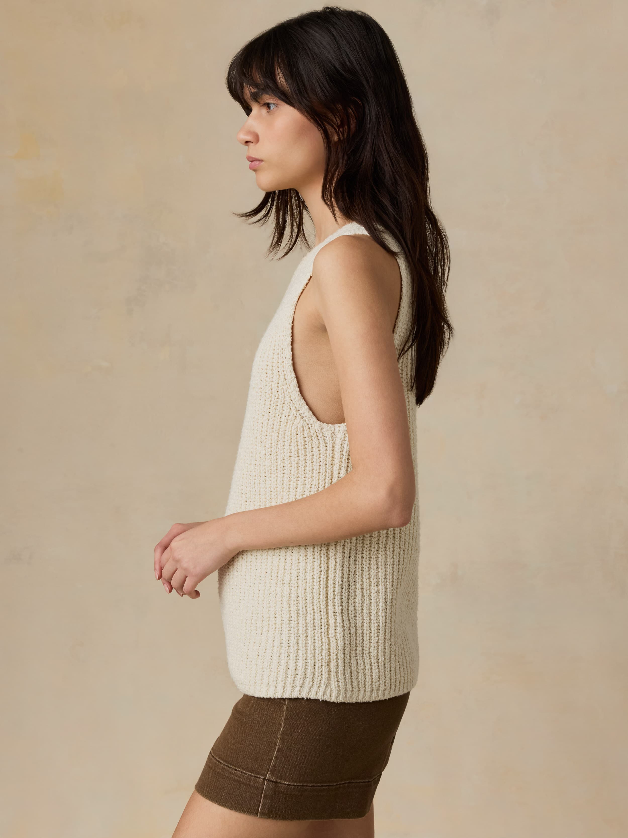 Woman wearing a beige knitted tank top against a beige background