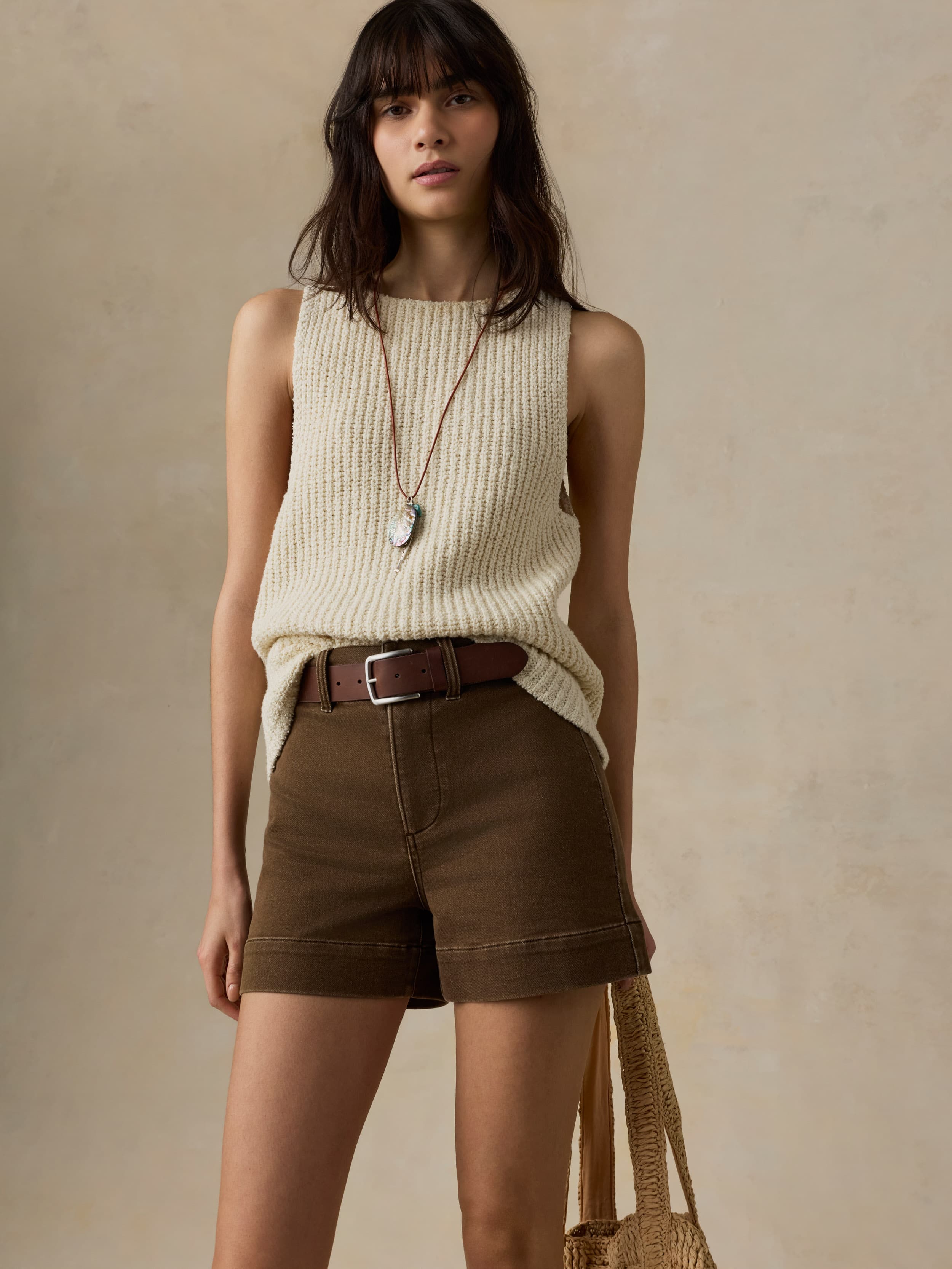 Woman wearing a beige sleeveless top and brown shorts against a neutral background