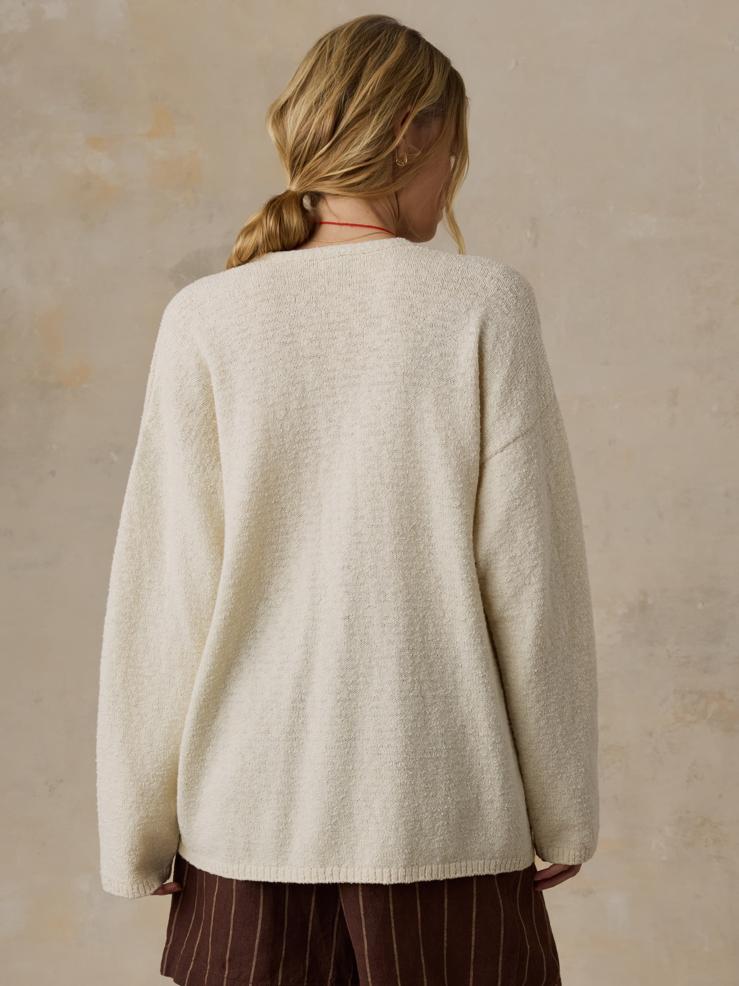 Woman wearing a cream sweater and brown striped shorts against a beige background