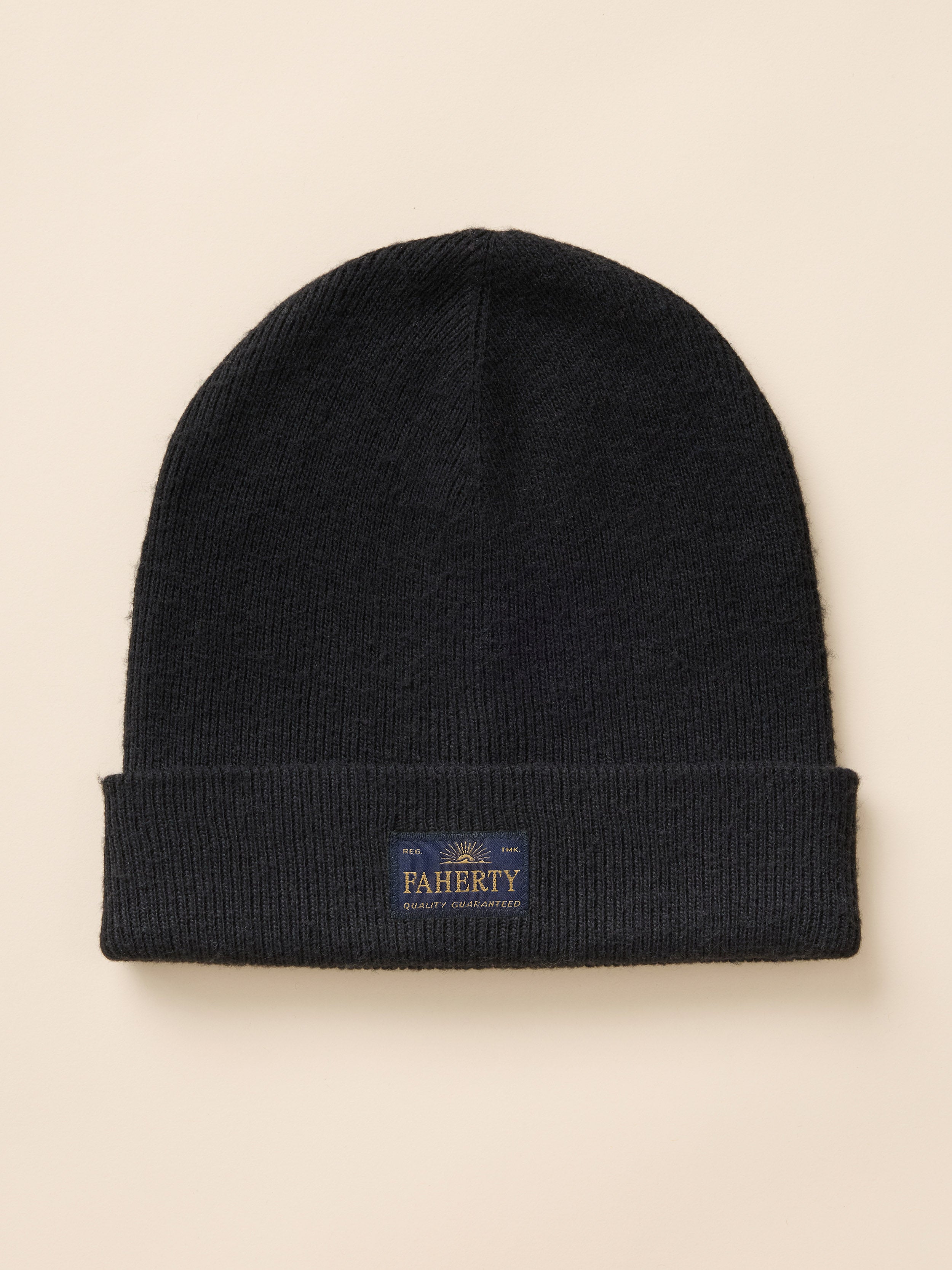 A black ribbed knit beanie hat with a folded cuff and logo patch, photographed flat against a light beige background.
