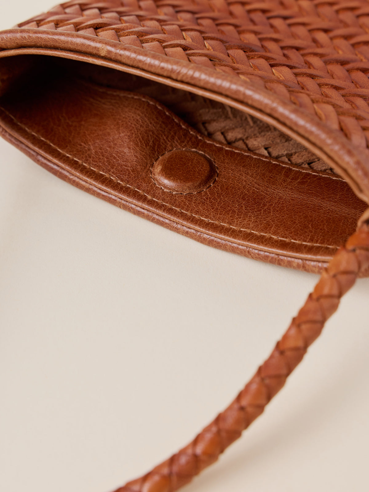Close-up of a brown woven leather bag showing the interior lining, a snap closure, and part of the braided strap on a light beige background., image 3 of 3