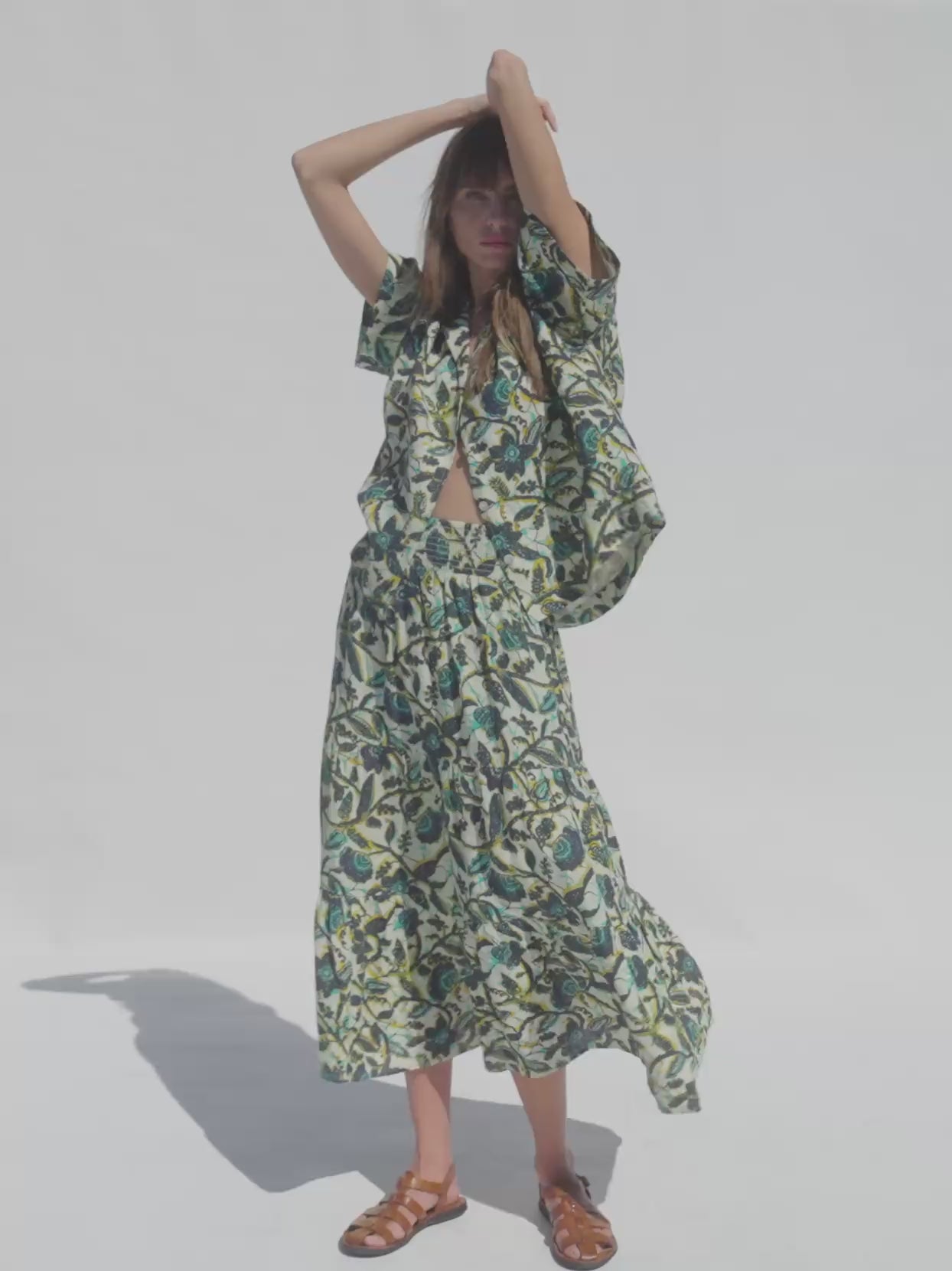 Video of a woman wearing a tropical print shirt and matching skirt against a white background