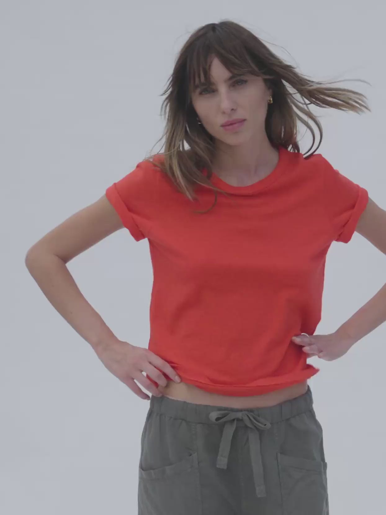 Video of a woman wearing a poppy red t-shirt with linen pants against a white background