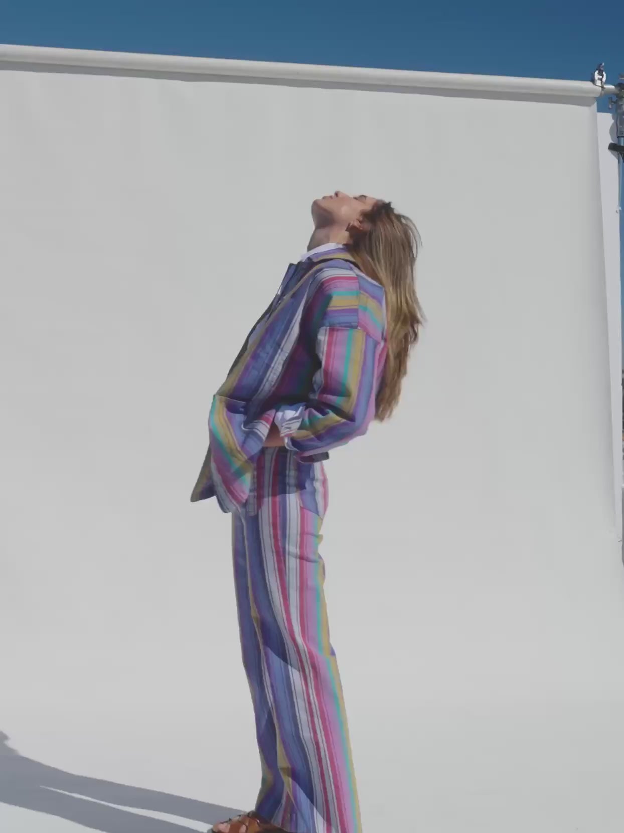 Video of a woman wearing a colorful striped suit against a beige background