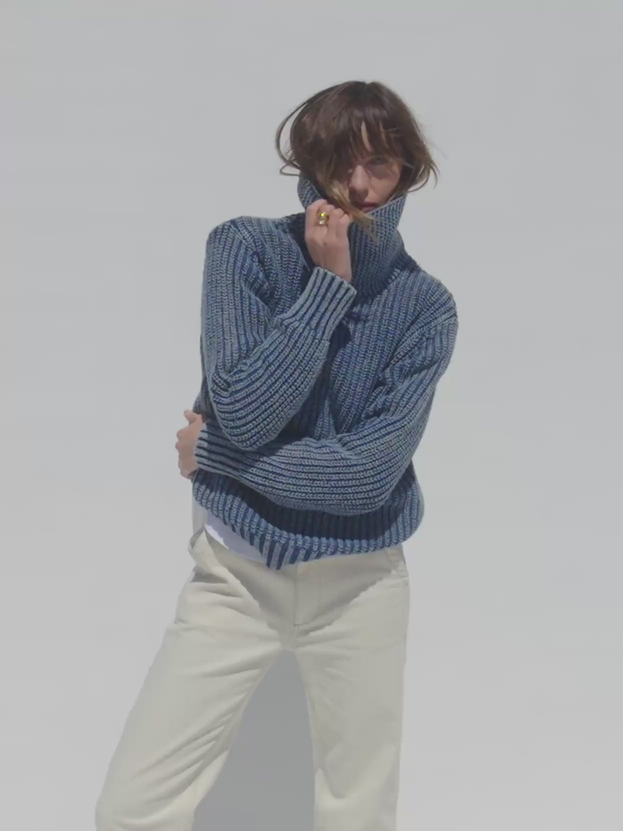 Video of a woman wearing a blue sweater and white pants against a white background
