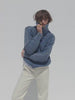 Video of a woman wearing a blue sweater and white pants against a white background