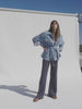 Video of a woman wearing a denim safari jacket and striped knit pants against a beige background