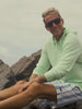 Man wearing a green hoodie and blue striped swim trunks at the beach
