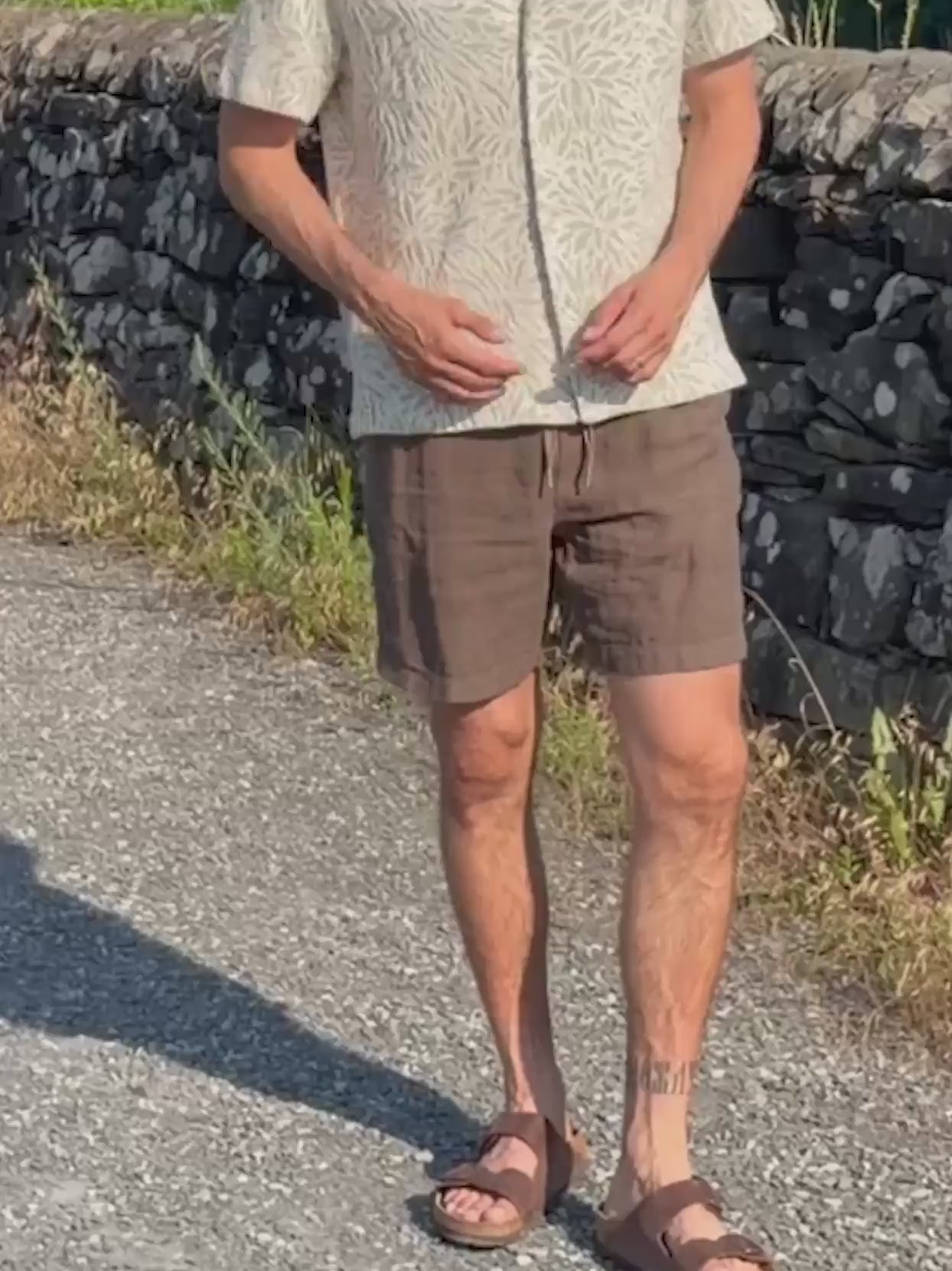 Man wearing a floral patterned shirt and brown linen shorts walking outside