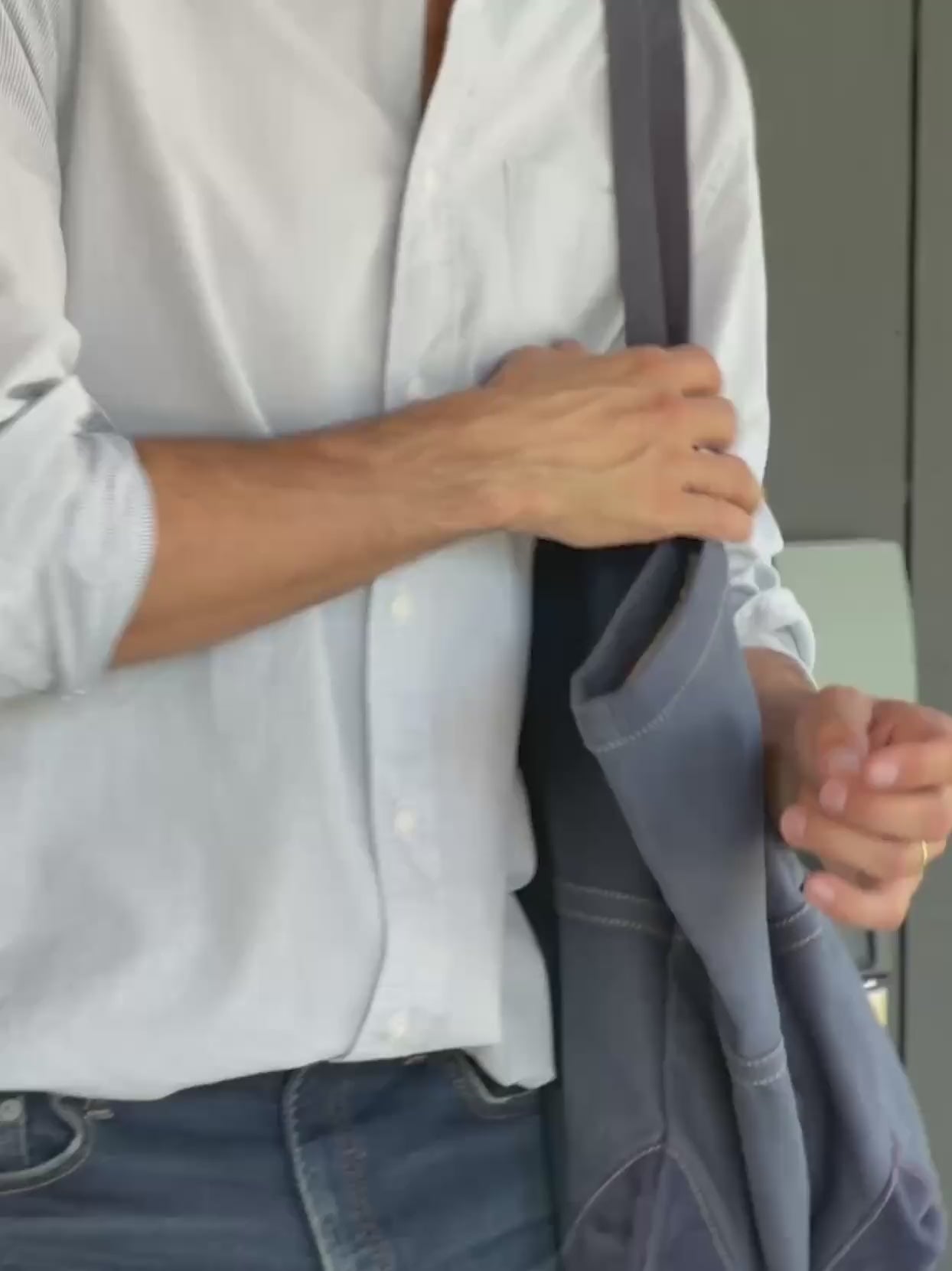 Man wearing a blue and white striped button down shirt and jeans holding a blue bag
