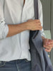 Man wearing a blue and white striped button down shirt and jeans holding a blue bag 