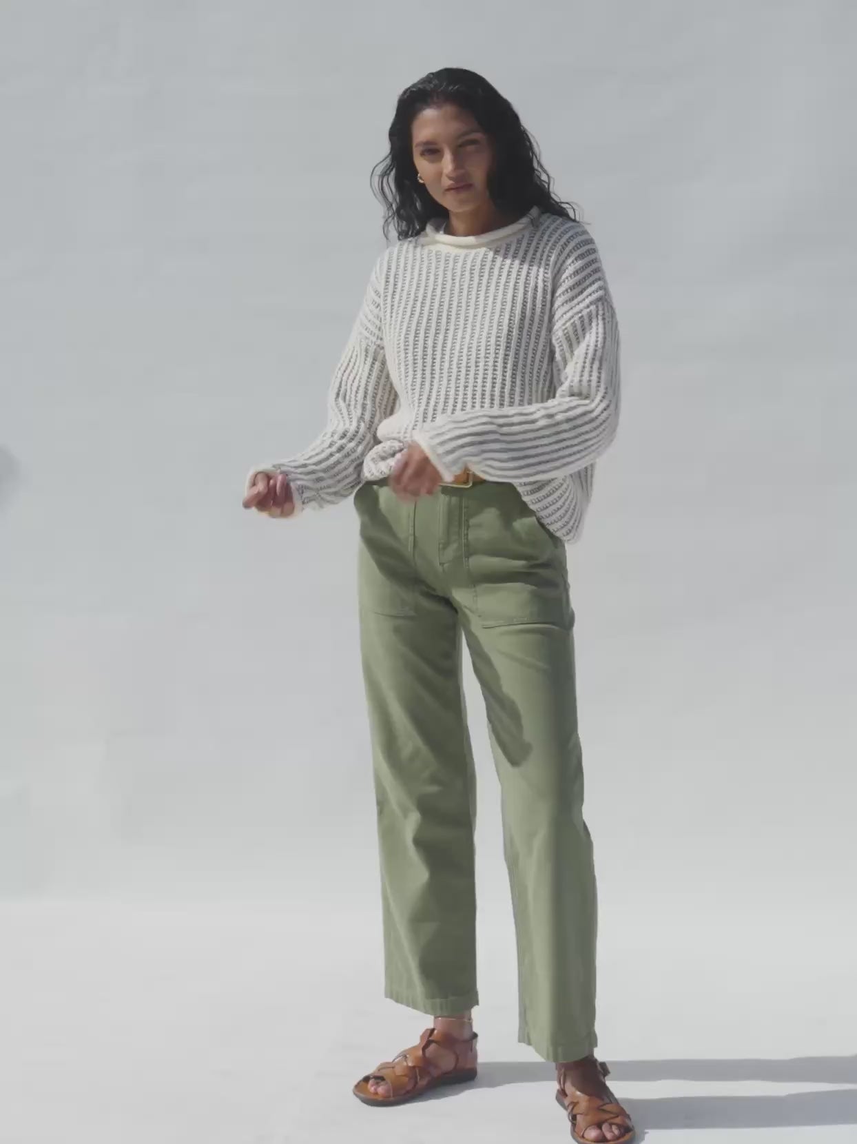Video of a woman wearing olive pants with a white sweater against a white background