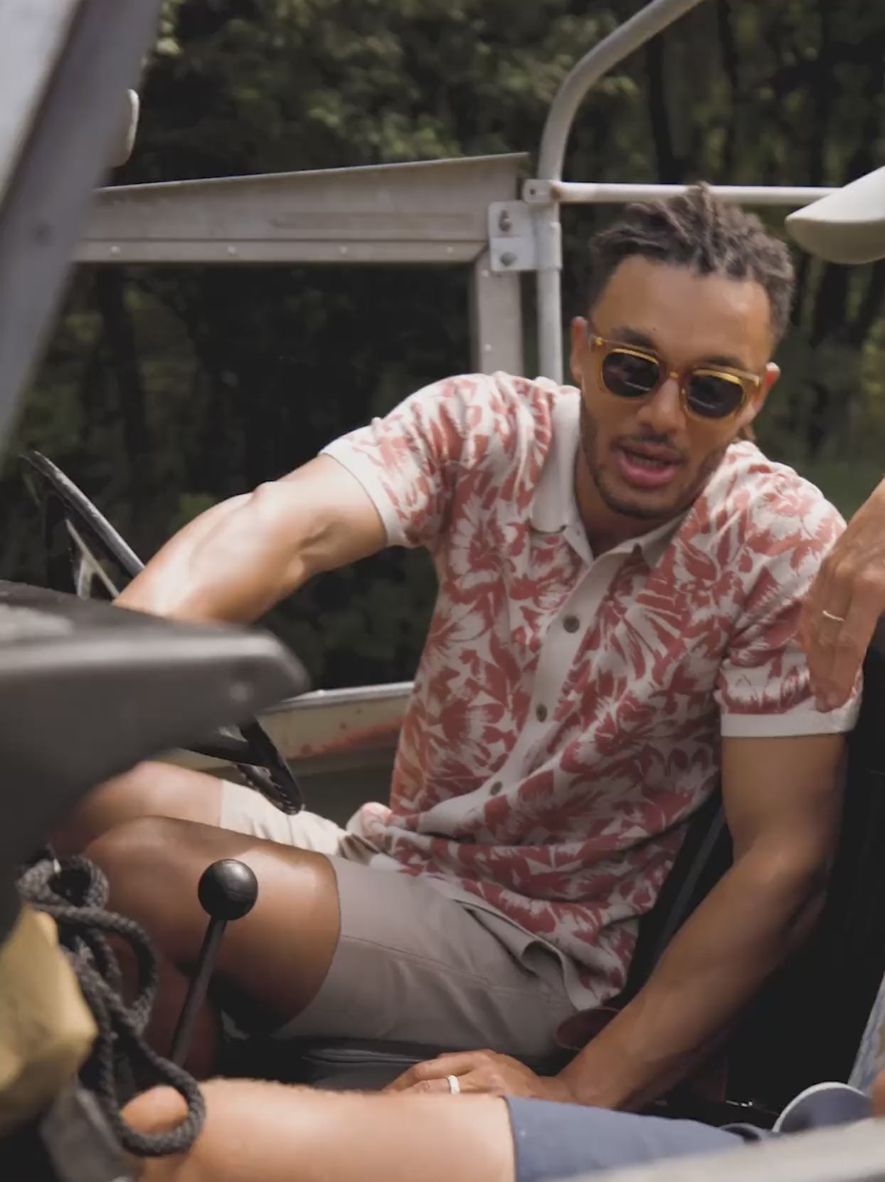 Video of a man wearing a printed short sleeve shirt sitting in a car.
