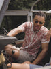 Video of a man wearing a printed short sleeve shirt sitting in a car.