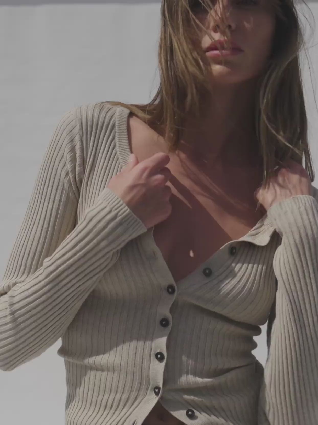 Video of a woman wearing a beige knit cardigan against a white background