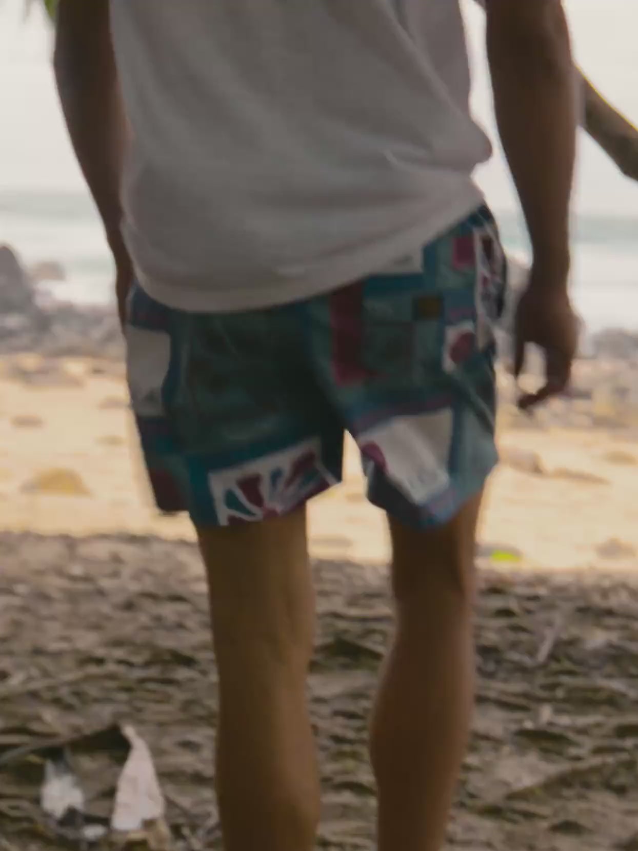 Man wearing a white henley and printed swim trunks at the beach