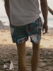 Man wearing a white henley and printed swim trunks at the beach