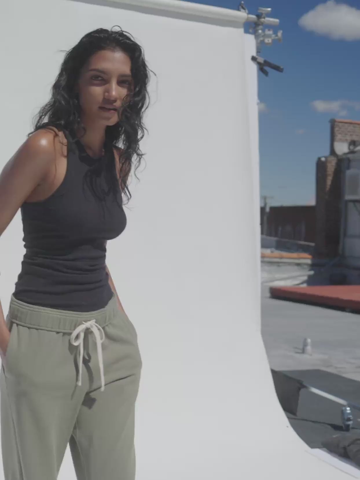 Video of a woman wearing a black tank top and green sweatpants against a white background
