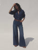 Video of a woman wearing a blue denim shirt and wide leg jeans against a white background