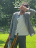 Man standing outside in the grass holding a chair while wearing a plaid shirt over a white tee and shorts 
