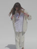 Video of a woman wearing a white button shirt, off white chore jacket, and matching pants against a white background