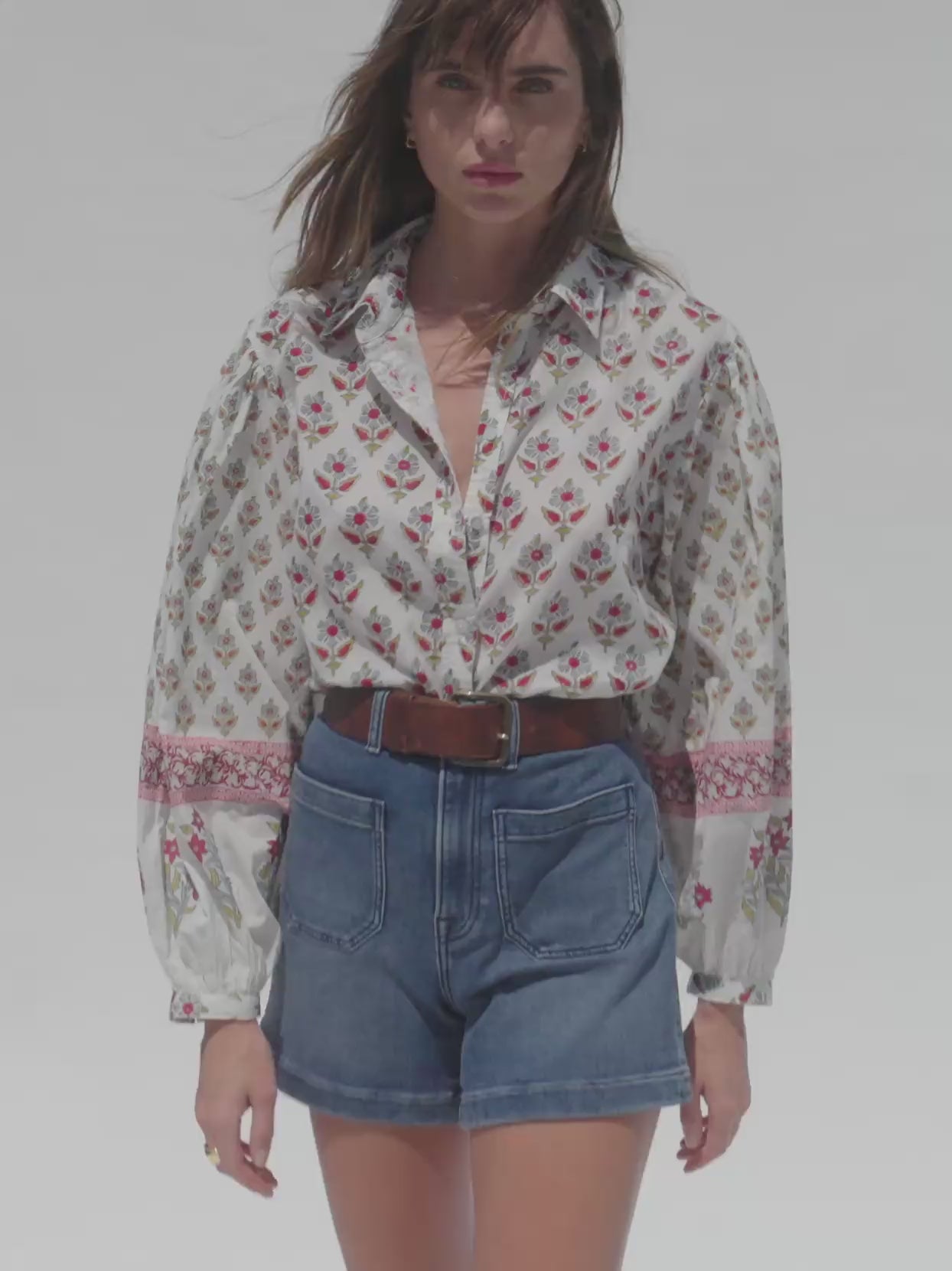Video of a woman wearing a floral blouse with blue denim shorts against a white background