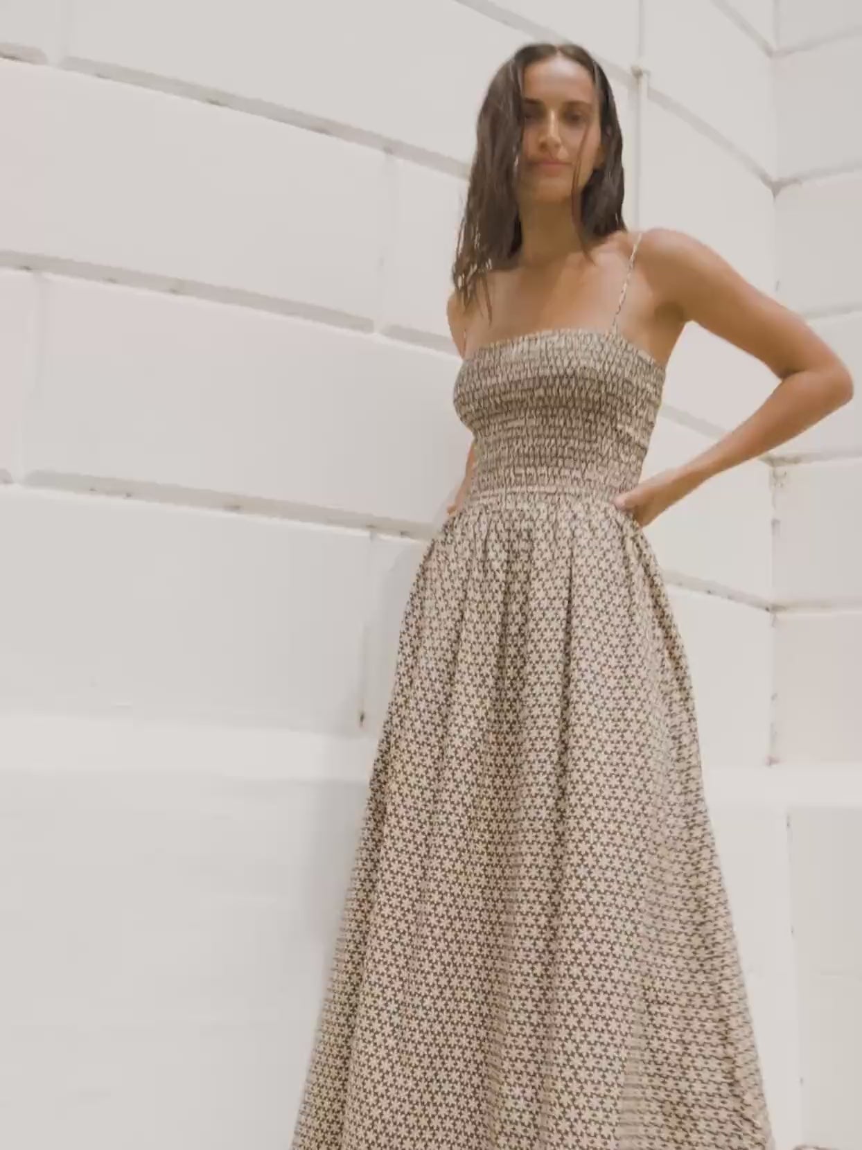 Video of a woman wearing brown floral patterned dress standing against a white wall