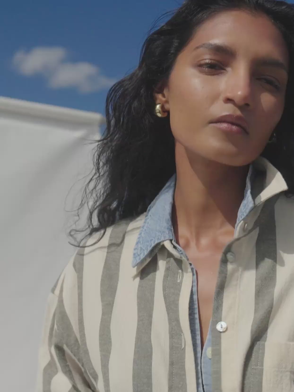 Video of a woman wearing a green striped linen shirt over a chambray shirt against a white background