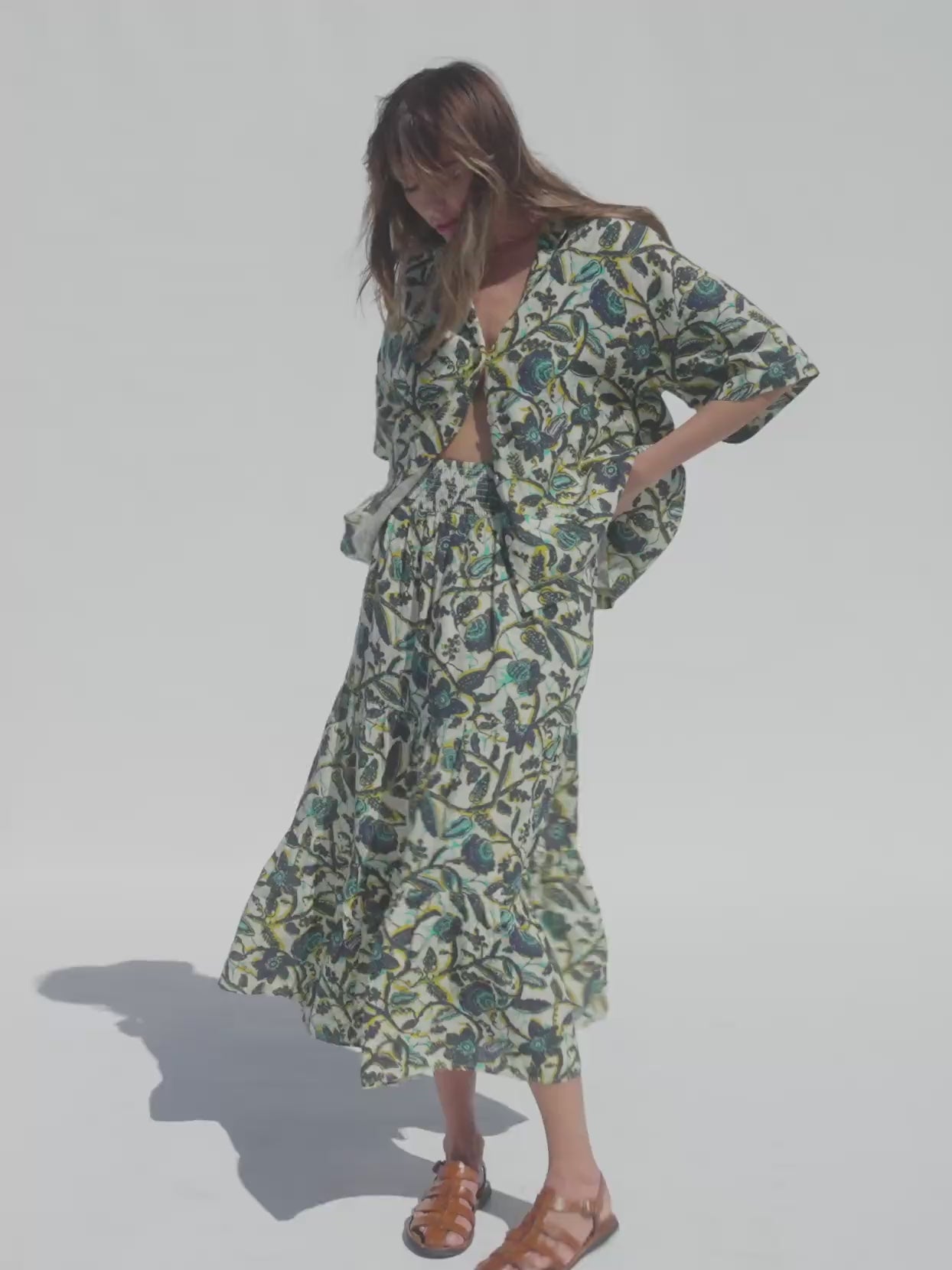 Video of a woman wearing a tropical print shirt and matching skirt against a white background