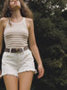 Video of a woman wearing a brown and white striped tank top and white denim shorts in a forest setting