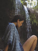 Video of a woman wearing a blue printed short sleeve shirt walking in the water.