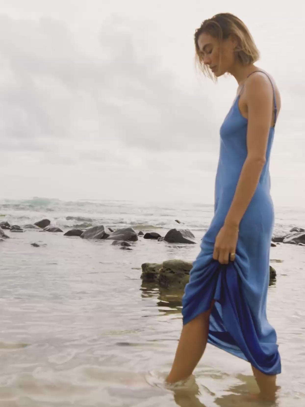 Video of a woman wearing a blue slip dress in the ocean water