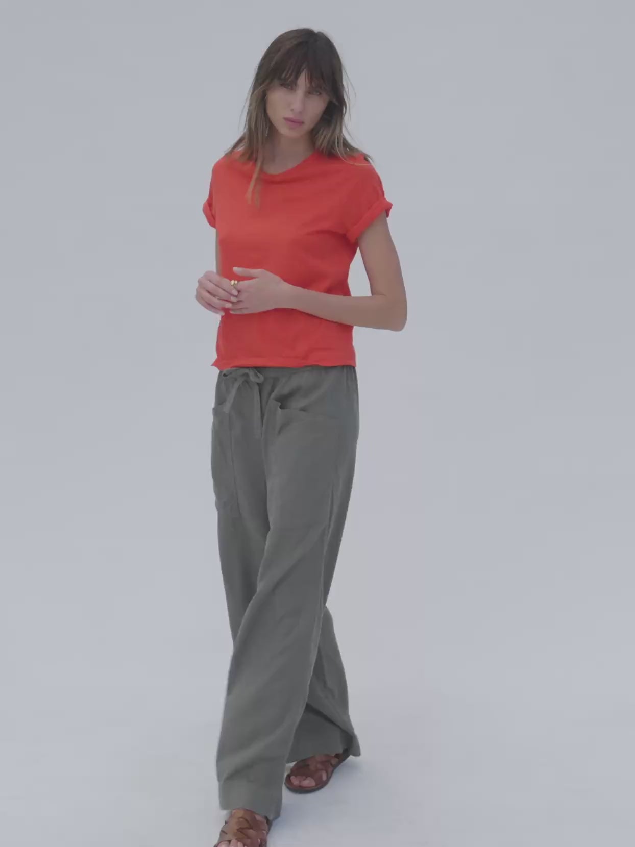 Video of a woman wearing a poppy red t-shirt with green linen pants against a white background