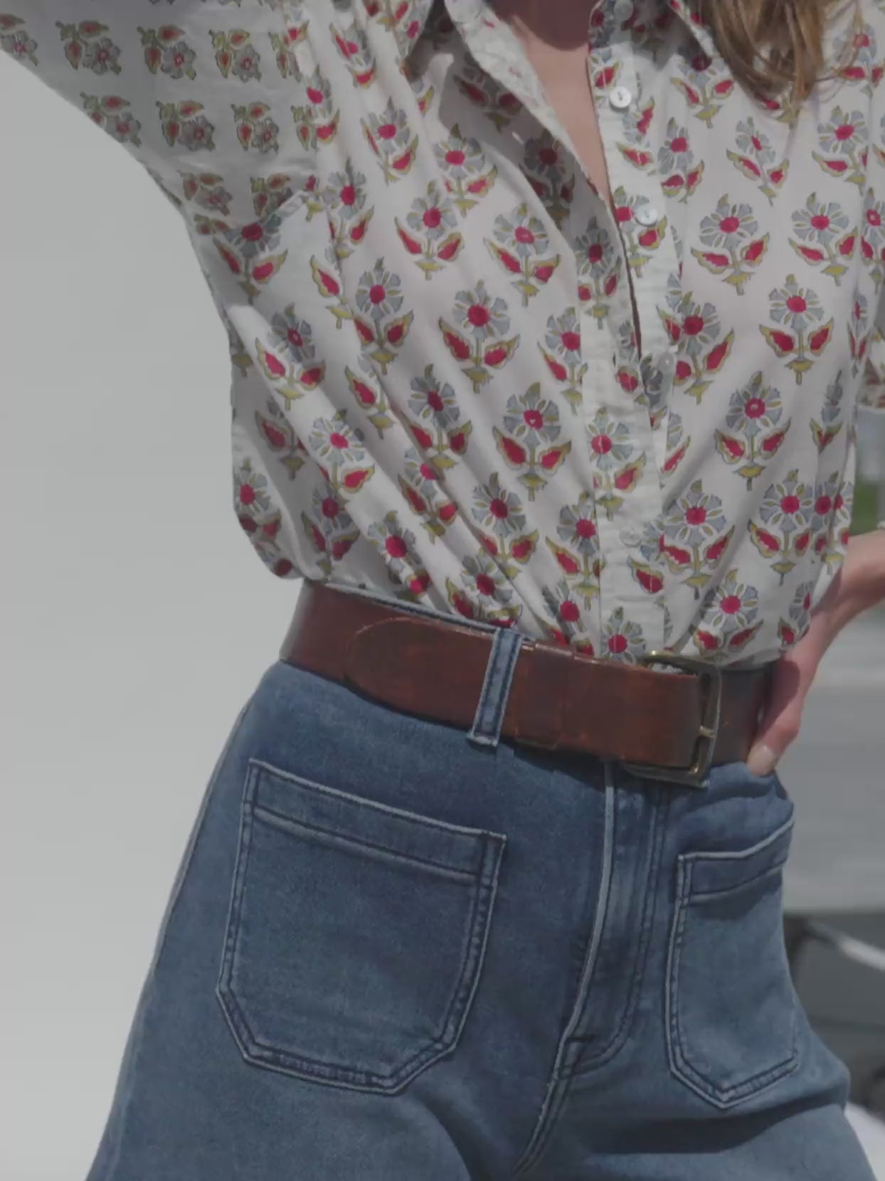Video of a woman wearing a floral print top and denim shorts against a white background