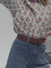 Video of a woman wearing a floral print top and denim shorts against a white background