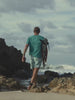 Man wearing a green t-shirt and green printed swim trunks surfing at the beach
