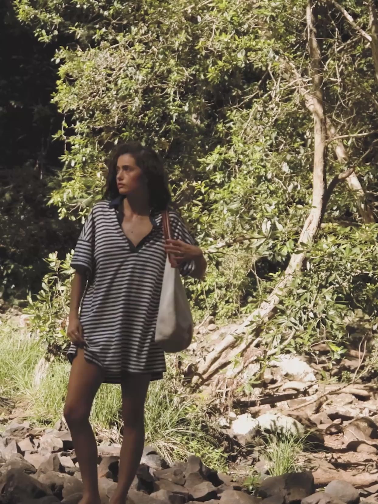 Video of a woman wearing a blue and white striped dress walking in a river.