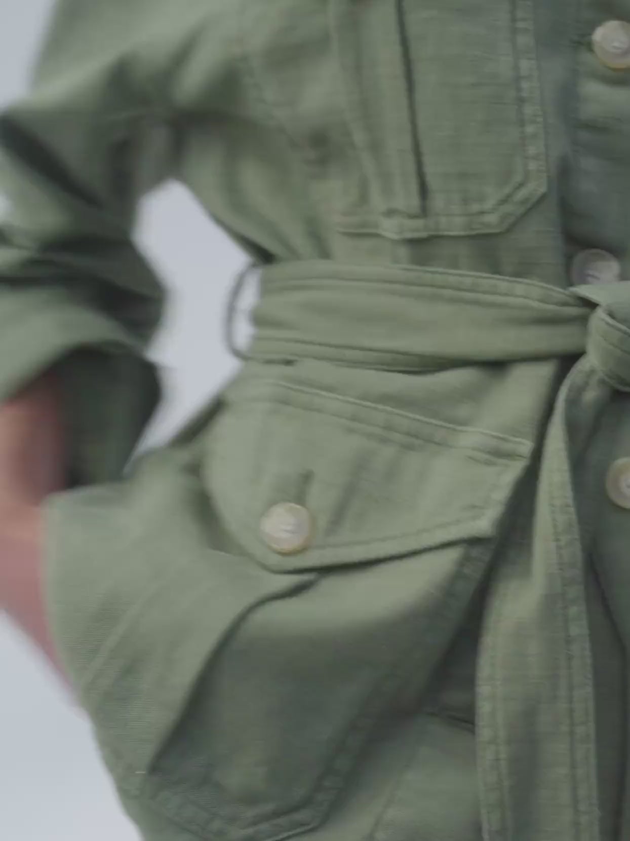 Video of a woman wearing a green safari jacket against a beige background