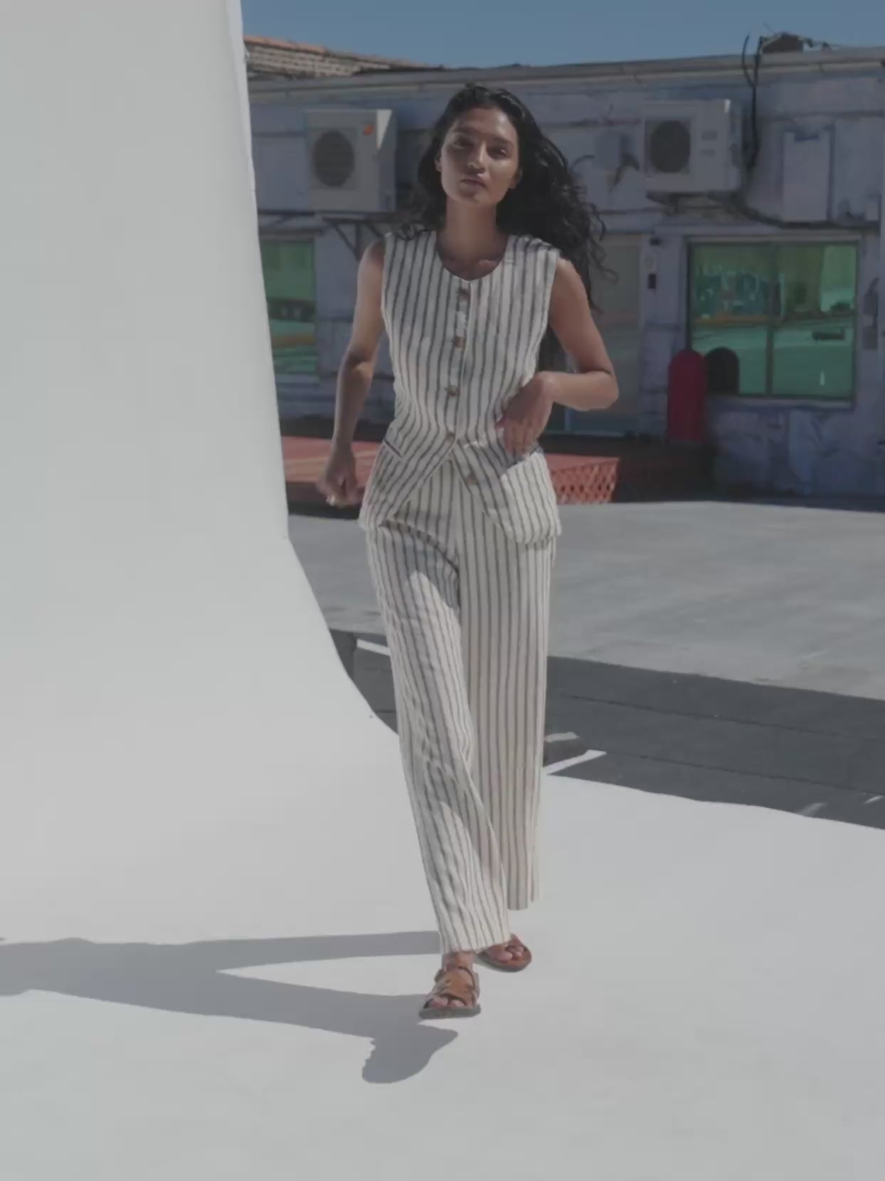 Video of a woman wearing a cream and brown striped linen vest and matching pants on a rooftop