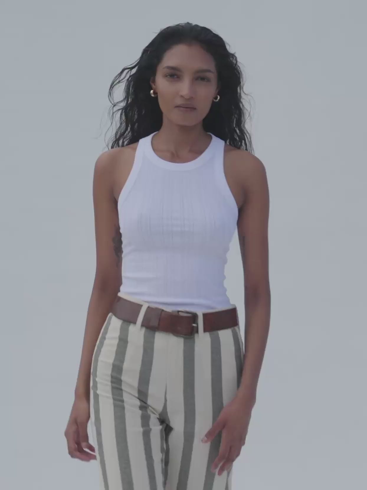 Video of a woman wearing a white tank top with green striped linen pants against a white background