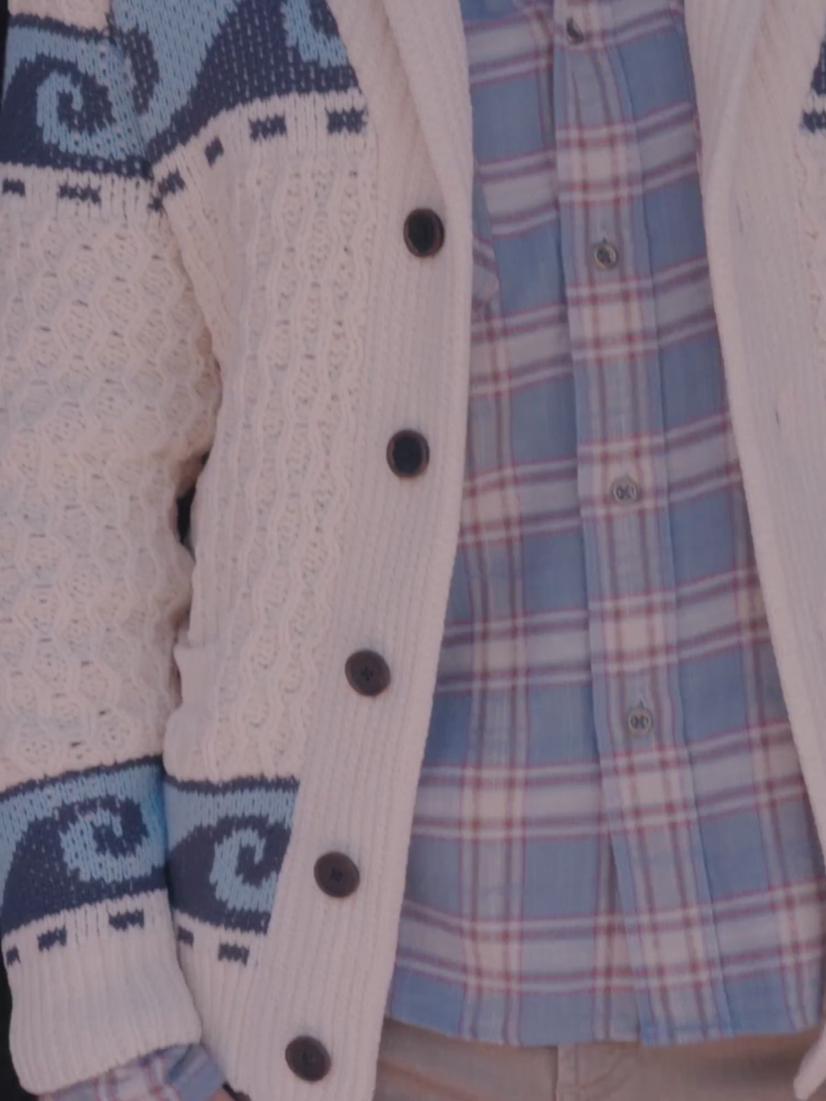 A man wearing a cream graphic cardigan over a button up shirt